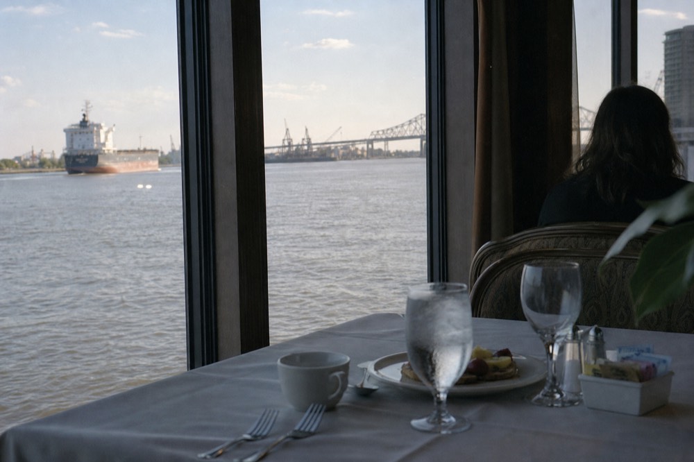 Riverboat brunch table set with white linen beside a large window looking out over the Mississippi in daylight
