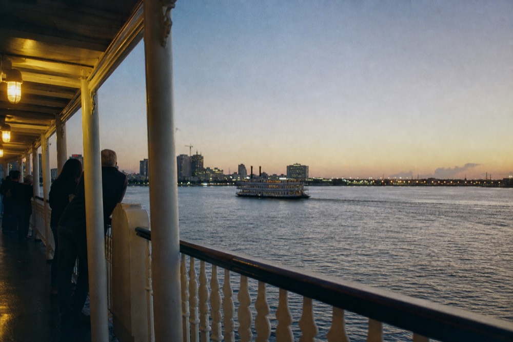 Passengers in light jackets standing at the rail of a riverboat upper deck under a clear autumn sky