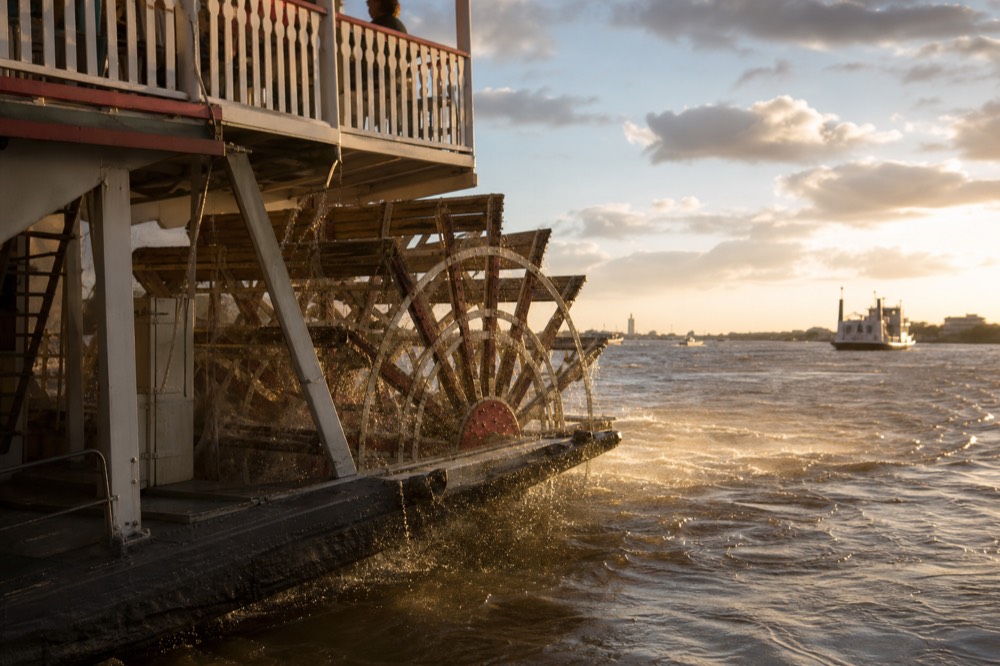 Golden late afternoon light on the paddlewheel of a sternwheeler churning brown river water