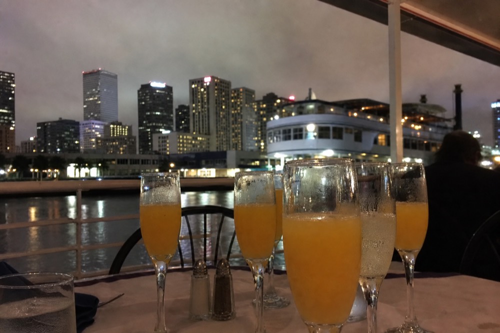 Row of mimosa flutes filled with orange juice and sparkling wine on a white linen riverboat brunch table