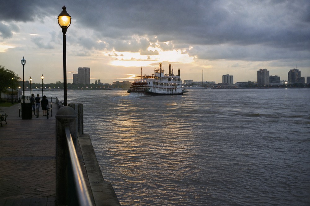 Dark storm clouds breaking over the Mississippi River with sunlight hitting the water and a paddlewheel riverboat in the middle distance