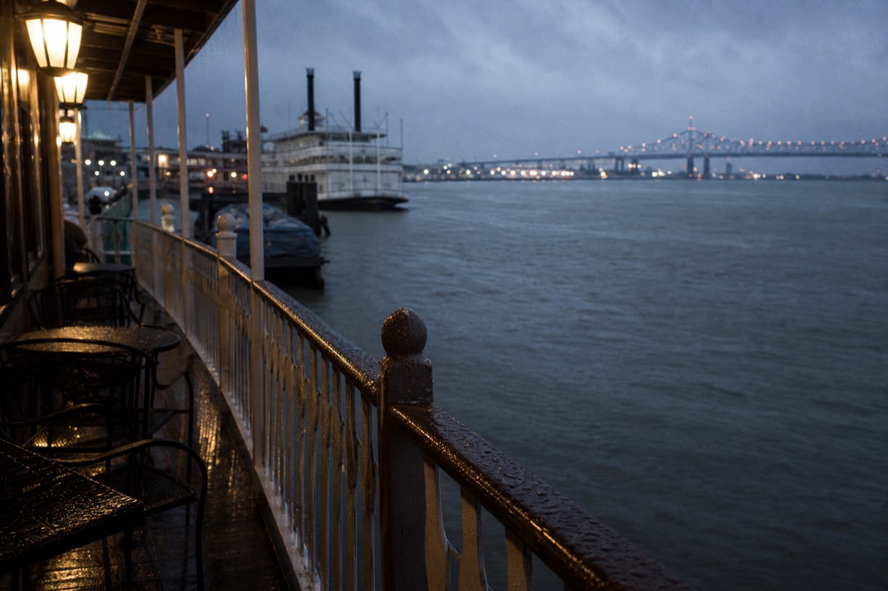 Rain falling on the Mississippi River beside a moored white riverboat, water beading on the deck railing and covered seating behind it