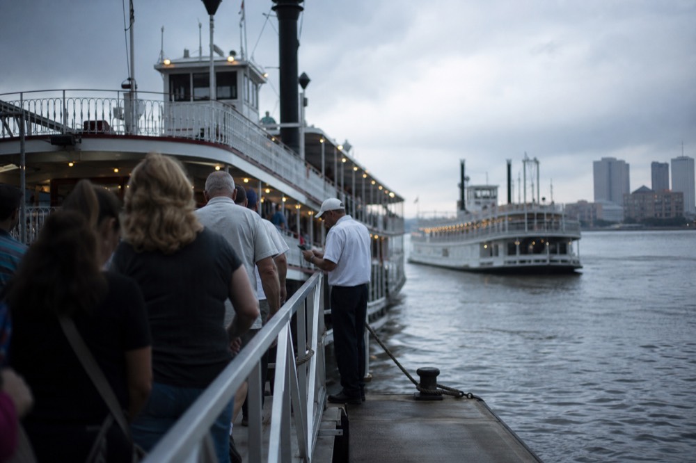 Passengers walking up a riverboat gangway in the evening while a crew member checks tickets at the rail