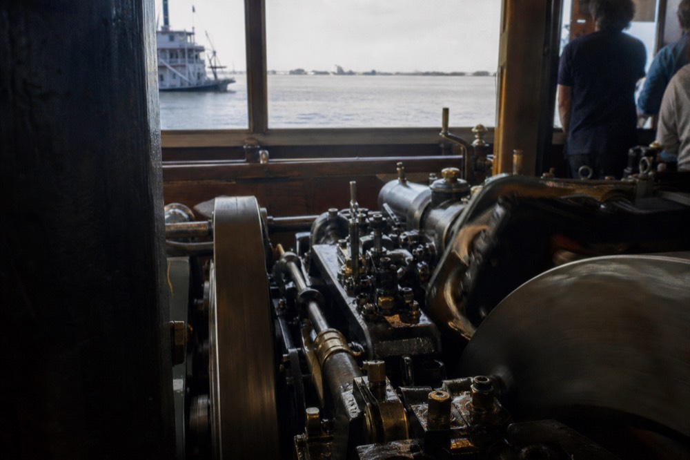 Brass and steel steam engine machinery in motion inside a riverboat engine room viewing area