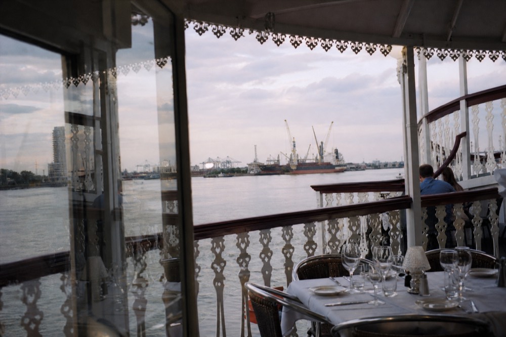 Ornate white riverboat deck railings and wooden trim with the Mississippi River and port cranes beyond