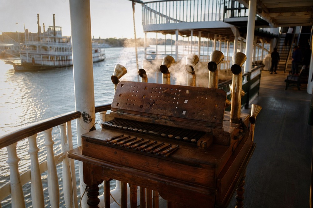 Steam calliope keyboard on the open deck of a riverboat with brass whistles venting steam behind it