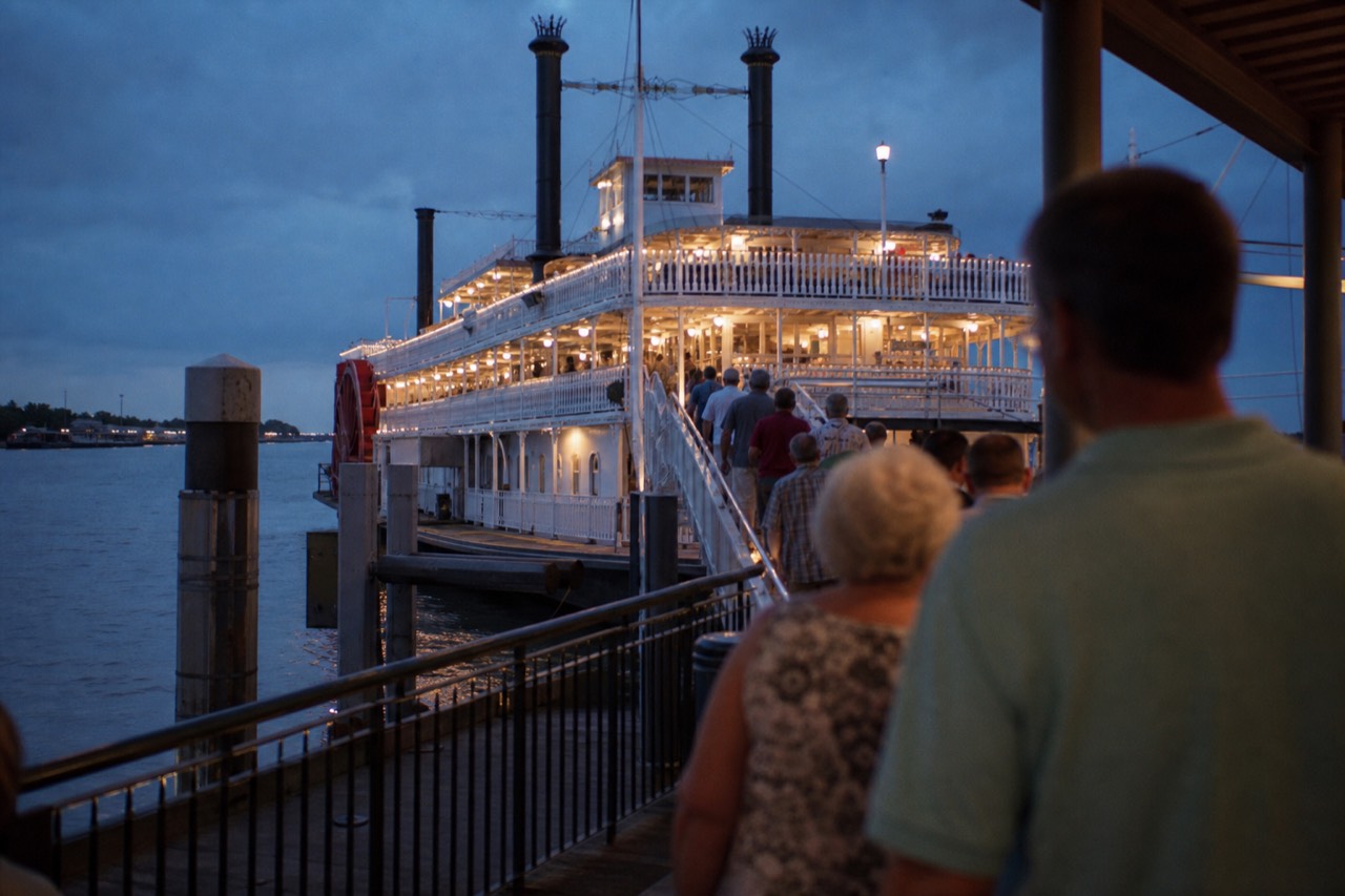 White steam sternwheeler seen from the riverfront promenade in New Orleans with passengers filing up the boarding ramp
