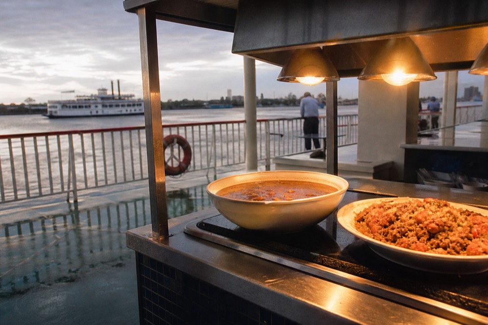 Bowl of gumbo and a plate of jambalaya on a riverboat buffet counter under warming lamps