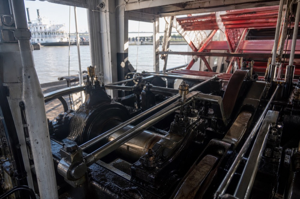 Polished steam engine rods and cranks driving a paddlewheel shaft inside a riverboat engine room