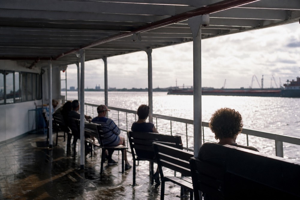 Shaded covered deck of a riverboat in summer with passengers sitting out of the sun and the river glaring beyond the rail
