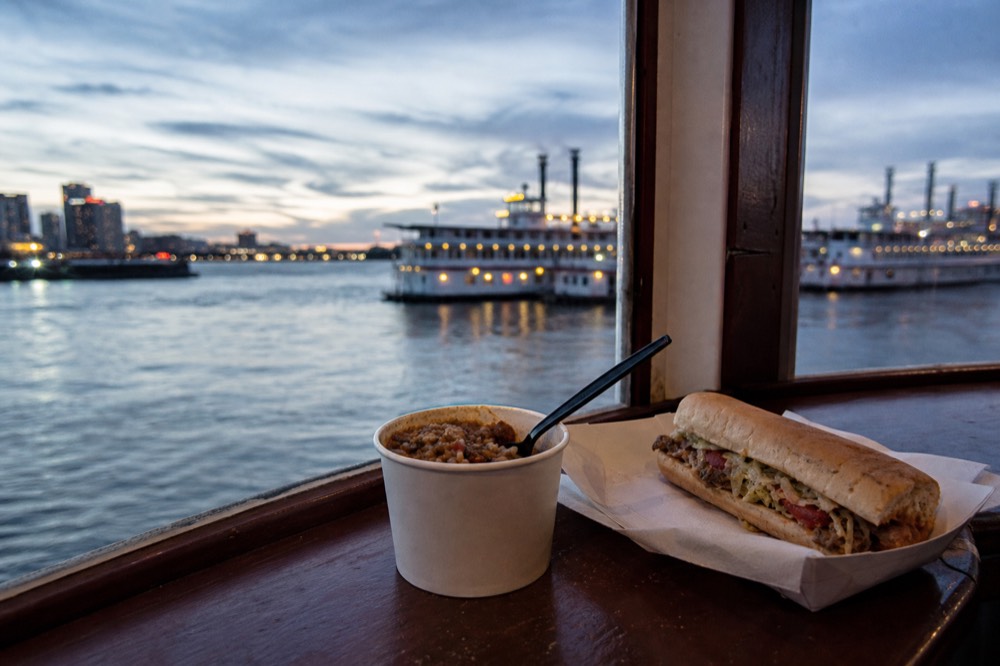 Paper cup of jambalaya and a po-boy on a riverboat bar counter with the river visible through the window