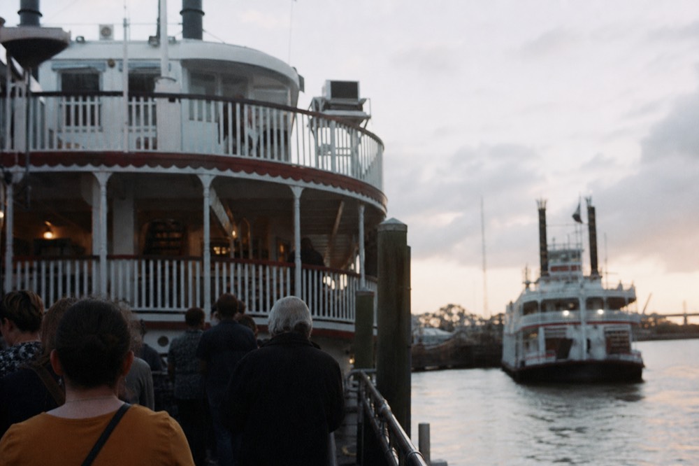 Passengers waiting at the Toulouse Street Wharf gangway at dusk with the sternwheeler's white superstructure above them