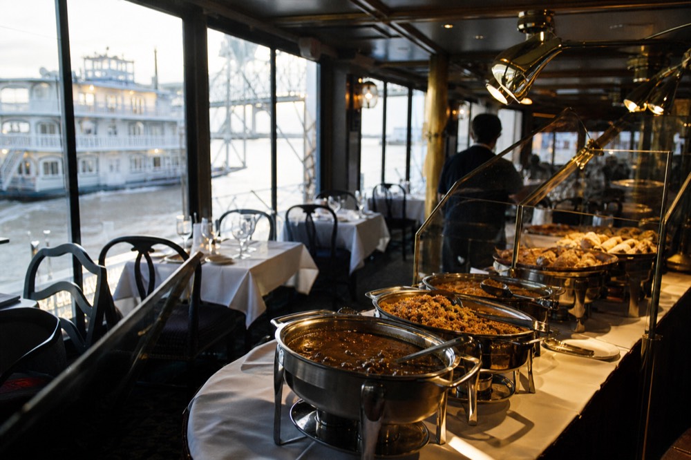 Creole buffet service line on a riverboat with gumbo tureens, jambalaya and carving station under warm lights