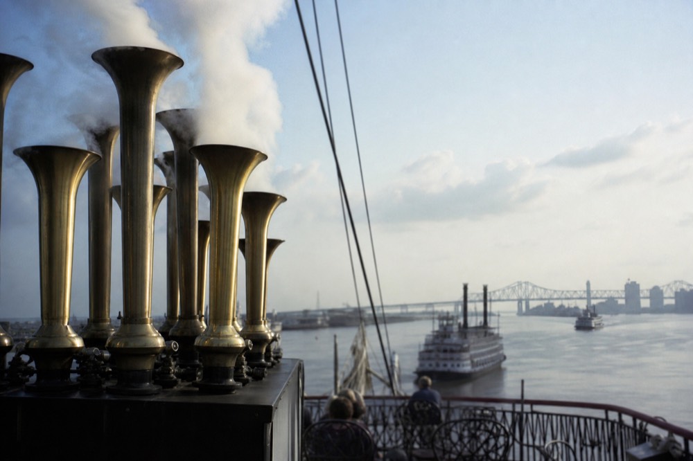 Brass steam calliope pipes on a riverboat deck venting white steam against a blue sky