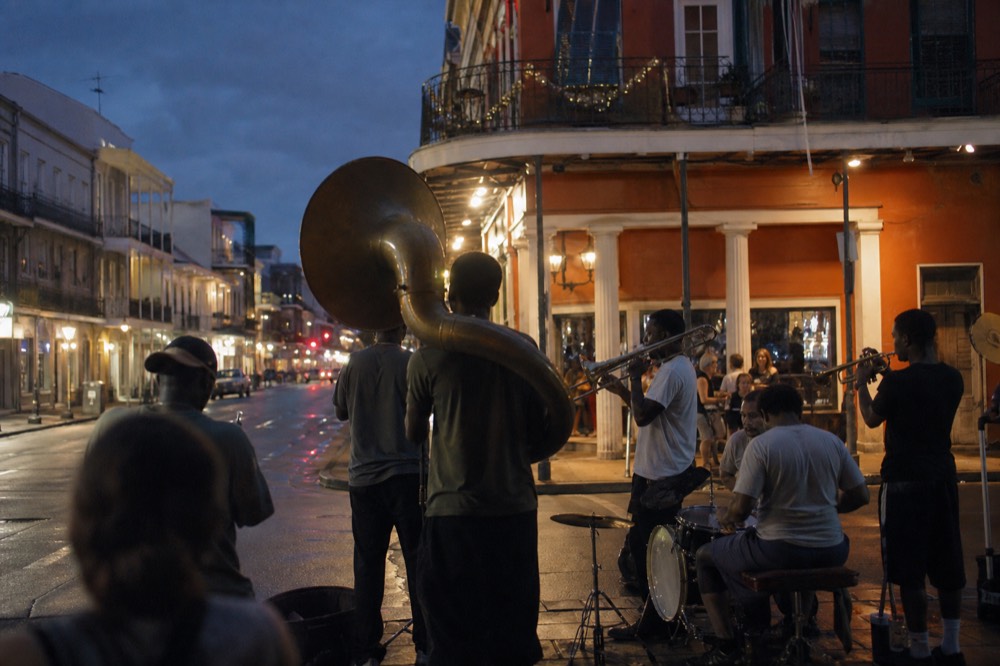 Lit French Quarter street at night with a brass band playing on the corner and people gathered on the pavement
