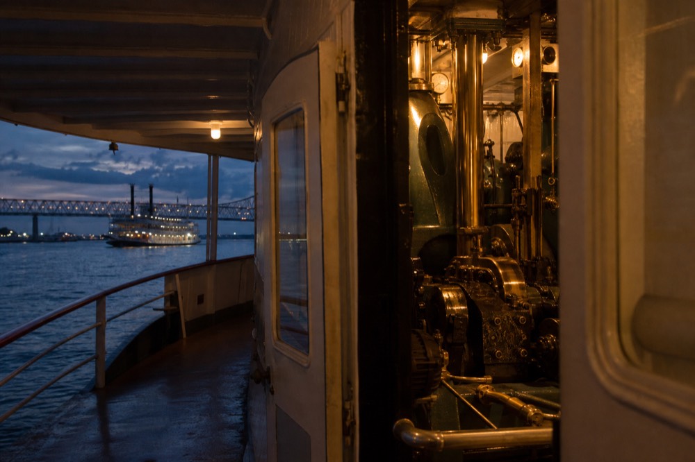 Polished brass and steel steam engine machinery visible through an open engine room doorway on a working riverboat