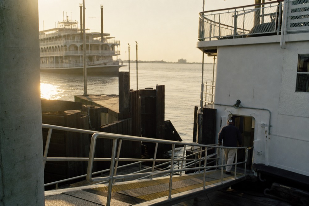 Wide riverboat gangway sloping from a concrete wharf down to an open boarding door on a white vessel