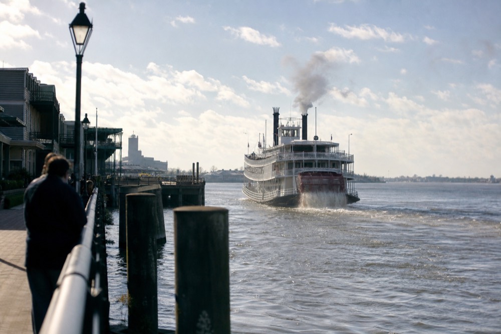 View from a levee walkway of a paddlewheeler pulling away from a French Quarter wharf on a bright morning