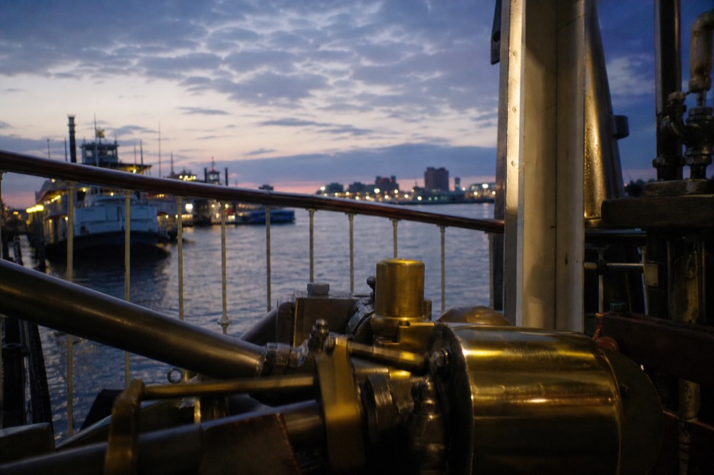 Brass and steel steam engine pistons turning behind a railing in a riverboat engine room viewing area