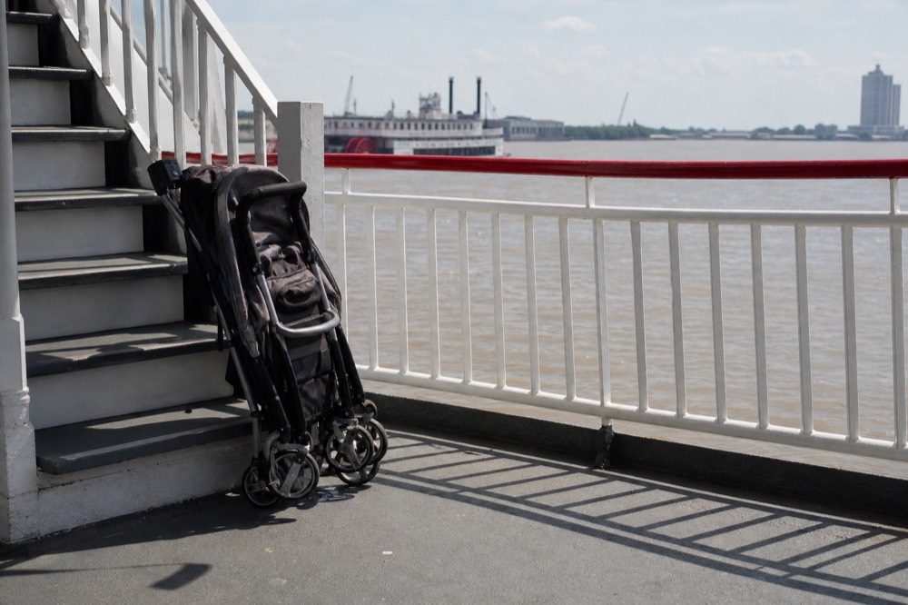 Folded stroller parked beside a white painted staircase on a riverboat deck with the river visible through the railing