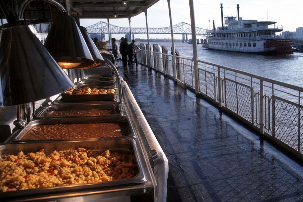 Riverboat buffet line with trays of jambalaya, red beans and bread pudding under warming lamps