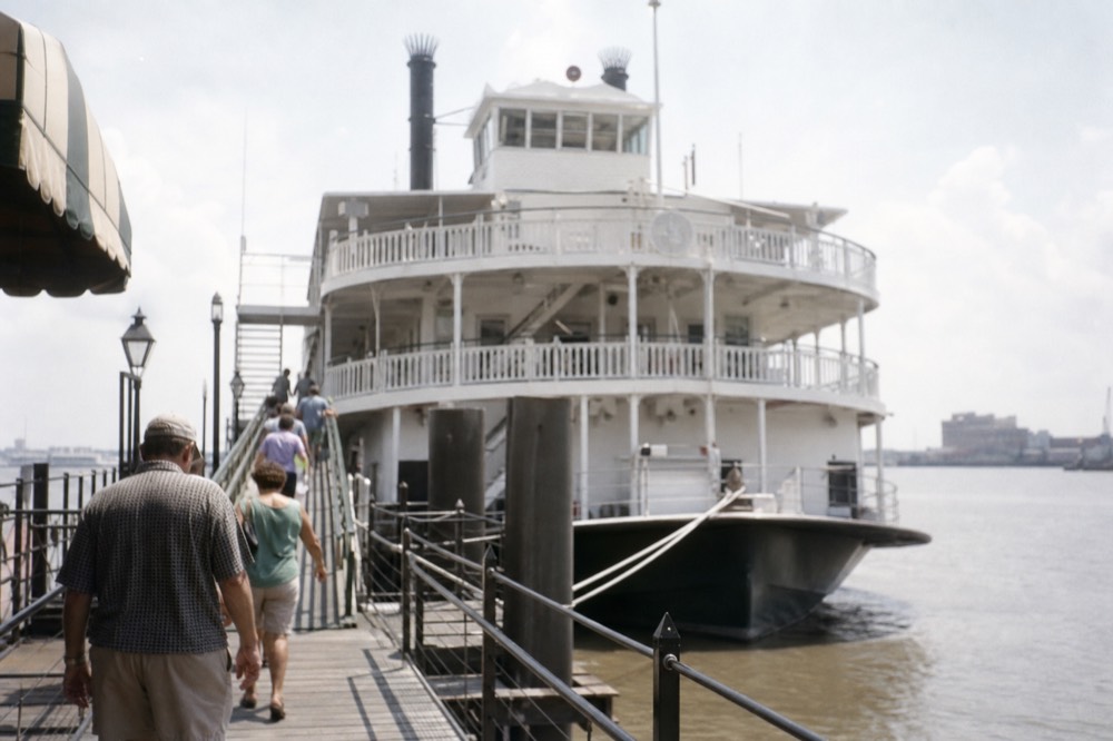 White riverboat moored at a wharf in late morning light with the gangway down and passengers walking aboard